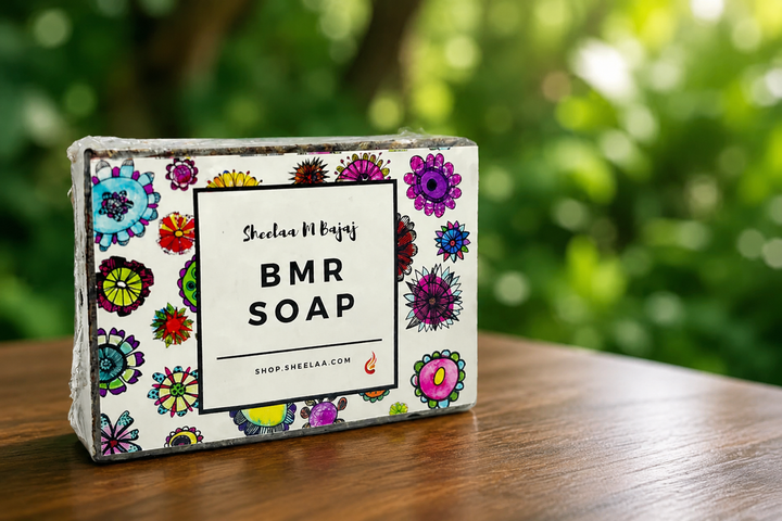 BMR Soap by House of Sheelaa displayed on a wooden surface with a natural green blurred background, showcasing vibrant floral packaging in a fresh artisanal wellness setting.
